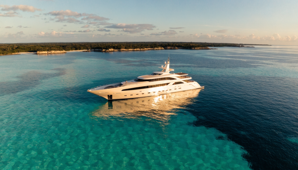 A white luxury superyacht anchored in calm turquoise water at golden hour