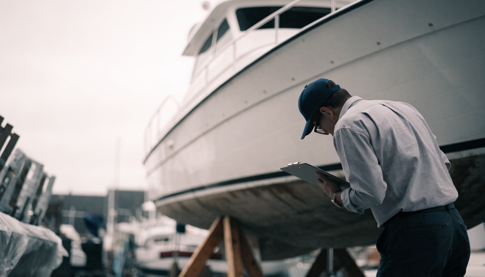 A marine surveyor inspecting the hull of a yacht hauled out on stands in a boatyard