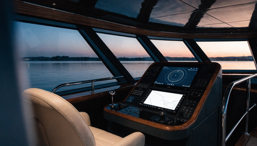 A modern superyacht helm station with glowing radar and chartplotter navigation displays at dusk