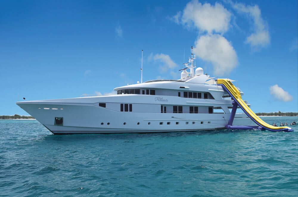 White superyacht at anchor in turquoise water with its water slide deployed, an MTS Yachts client vessel