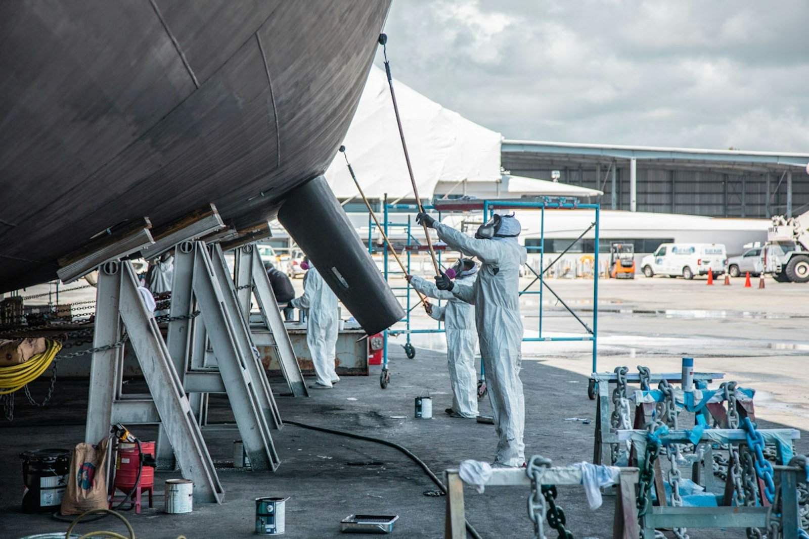 Yard workers in protective suits working beneath a hauled-out superyacht hull
